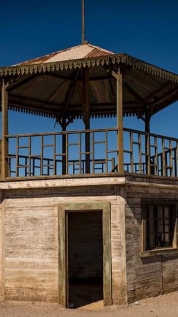 Glorieta de madera de dos pisos con baranda calada, bajo cielo azul oscuro