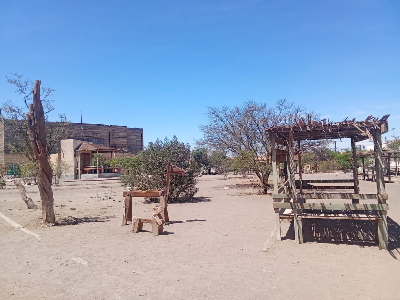 Plaza con un caballito de madera, árboles secos y una glorieta bajo cielo despejado